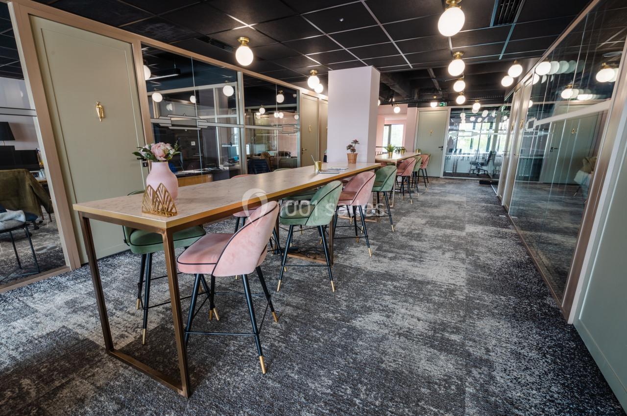 Salle de coworking moderne avec une longue table, chaises colorées, éclairage suspendu et cloisons vitrées.
