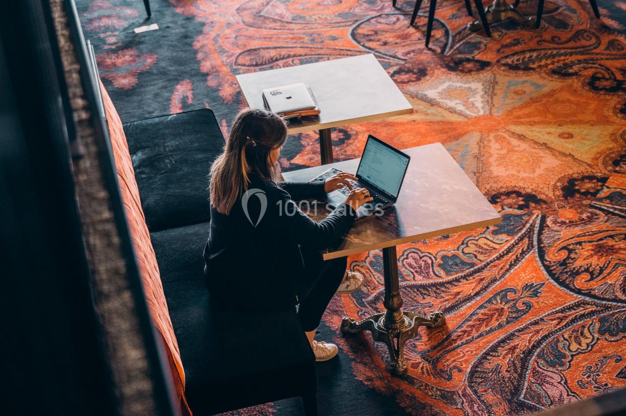 Une femme travaille sur un ordinateur portable, assise à une table dans un espace avec un tapis coloré.