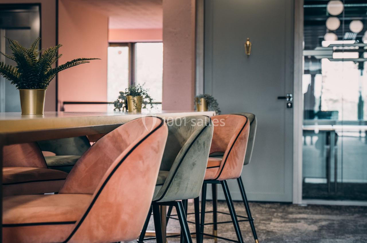 Chaises rembourrées roses et vertes autour d'une table en bois dans un espace intérieur lumineux et moderne.