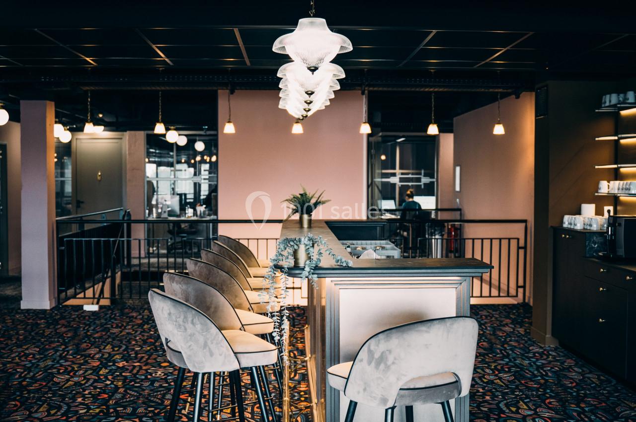 Bar élégant avec comptoir en bois clair, tabourets rembourrés, éclairage suspendu et décoration moderne.