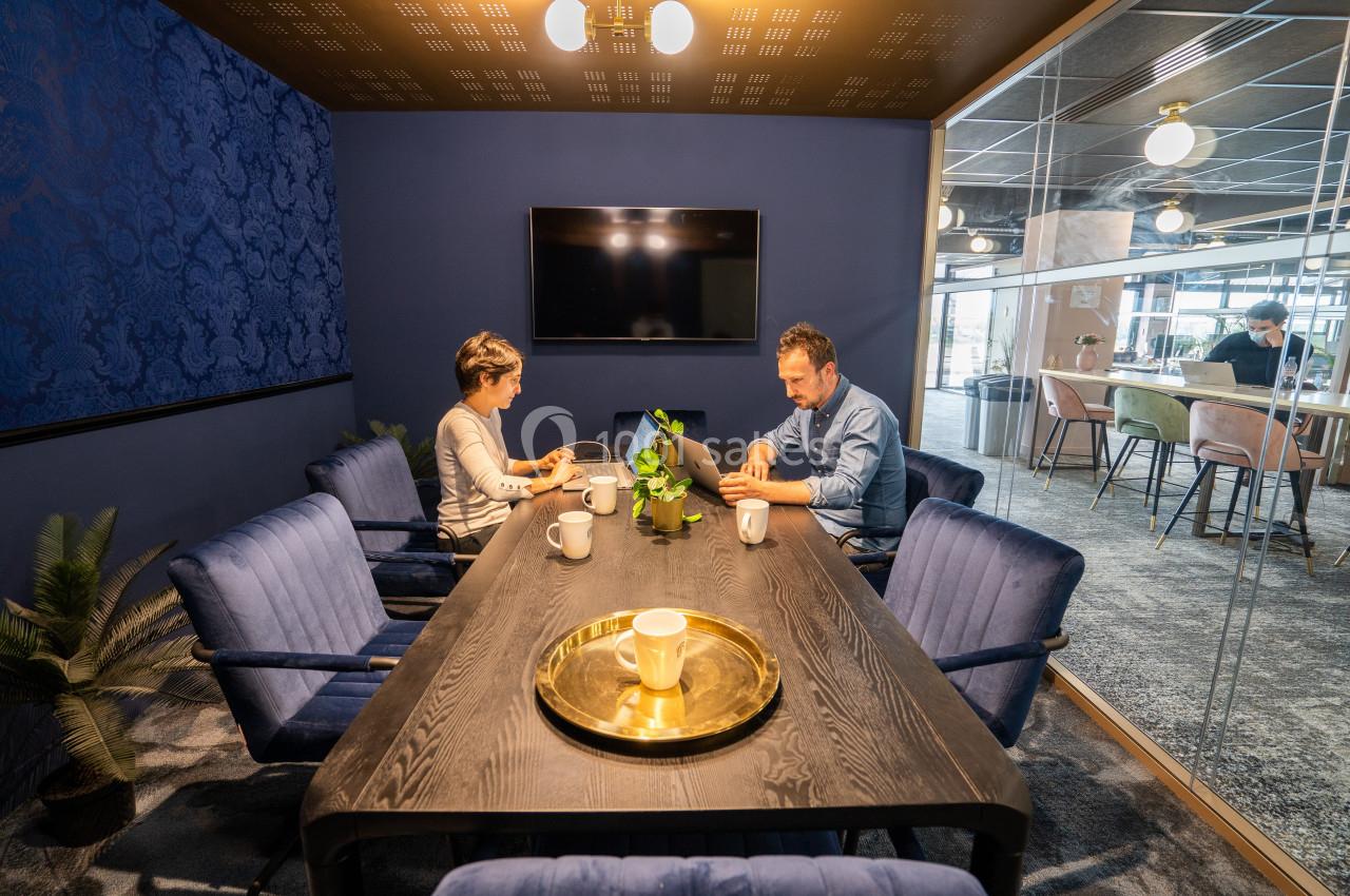Deux personnes travaillent sur des ordinateurs portables dans une salle de réunion moderne avec une table en bois sombre.