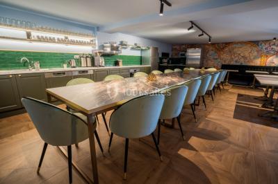 Salle de réunion avec table en bois foncé, six chaises grises, tableau blanc et écran mural.