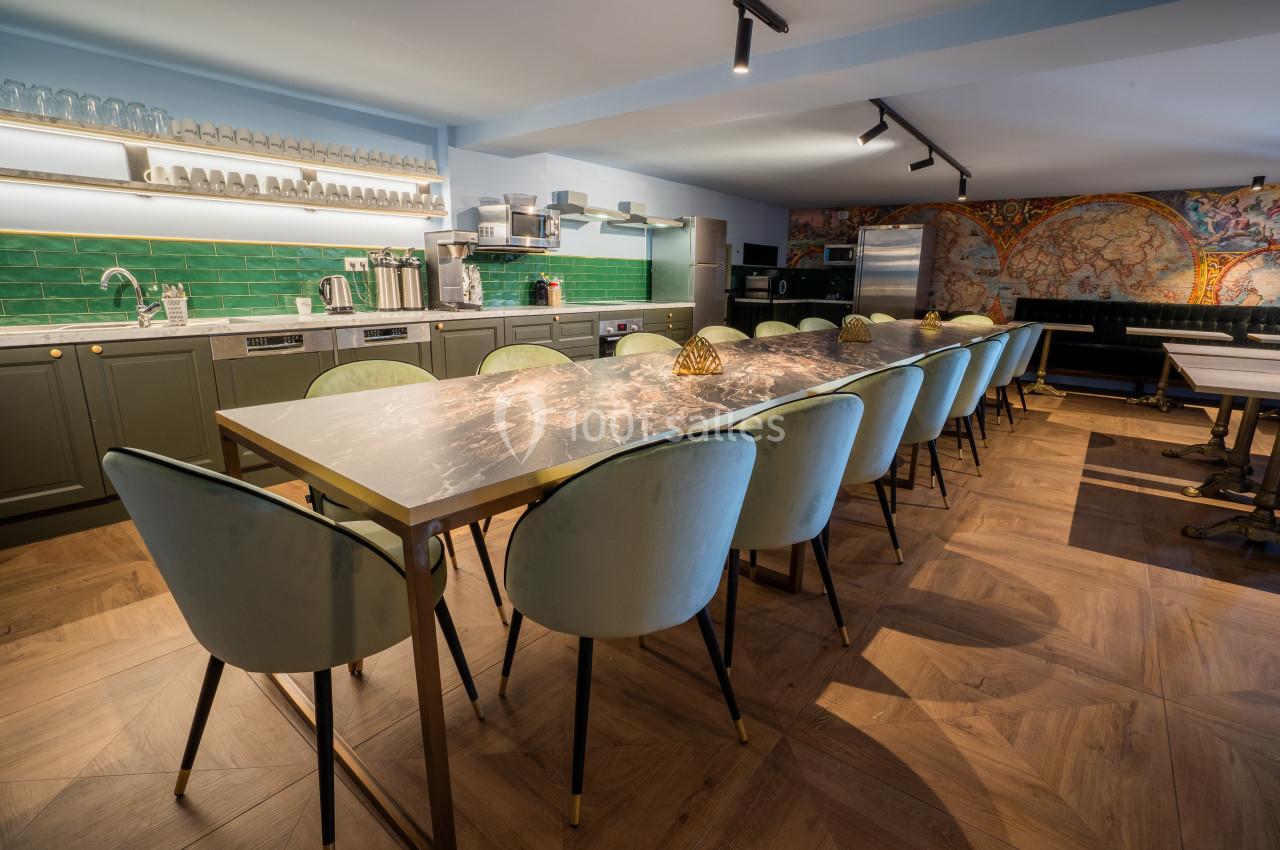 Grande table en marbre entourée de chaises rembourrées dans une cuisine moderne avec murs verts et étagères ouvertes.