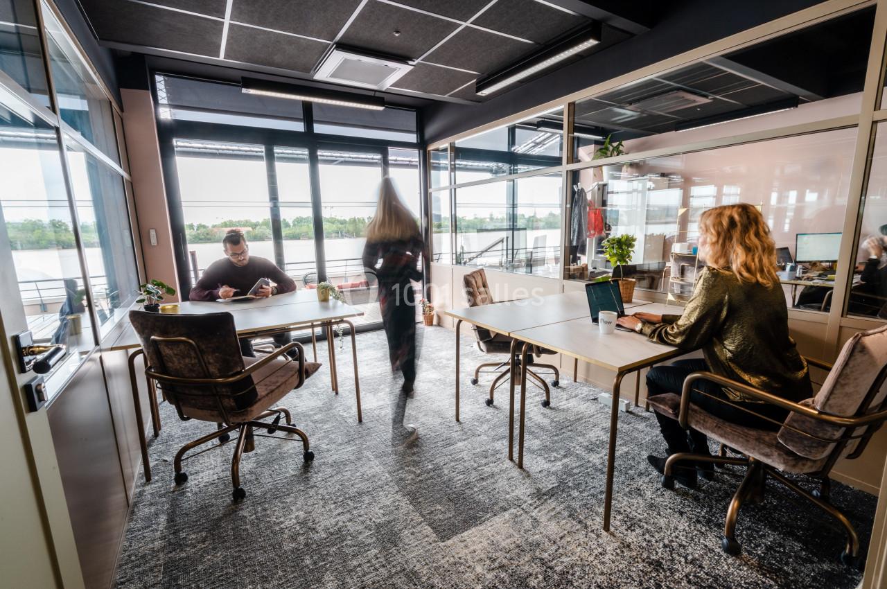 Personnes travaillant dans un bureau lumineux avec de grandes fenêtres donnant sur un paysage extérieur.