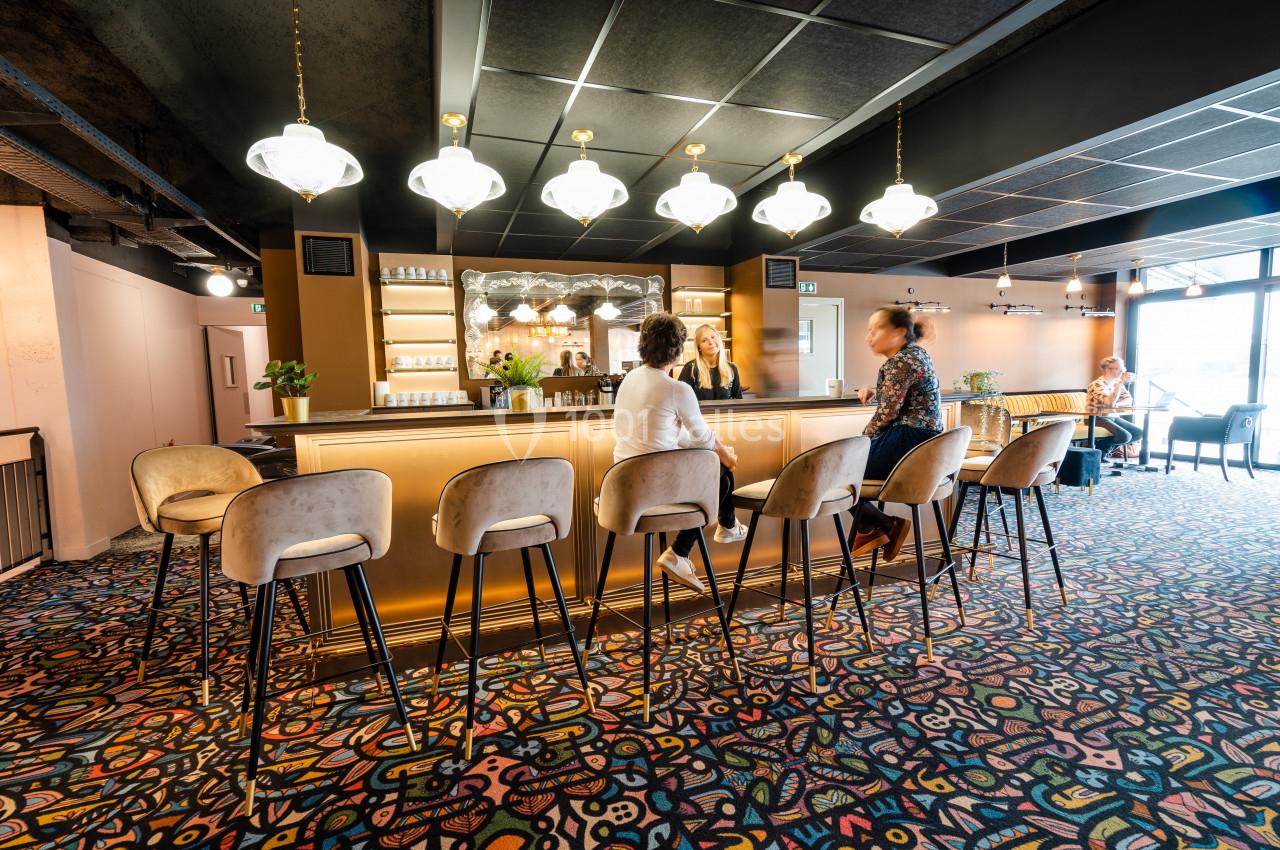 Un bar lumineux avec des tabourets hauts, des suspensions élégantes et des clients assis dans un décor coloré.