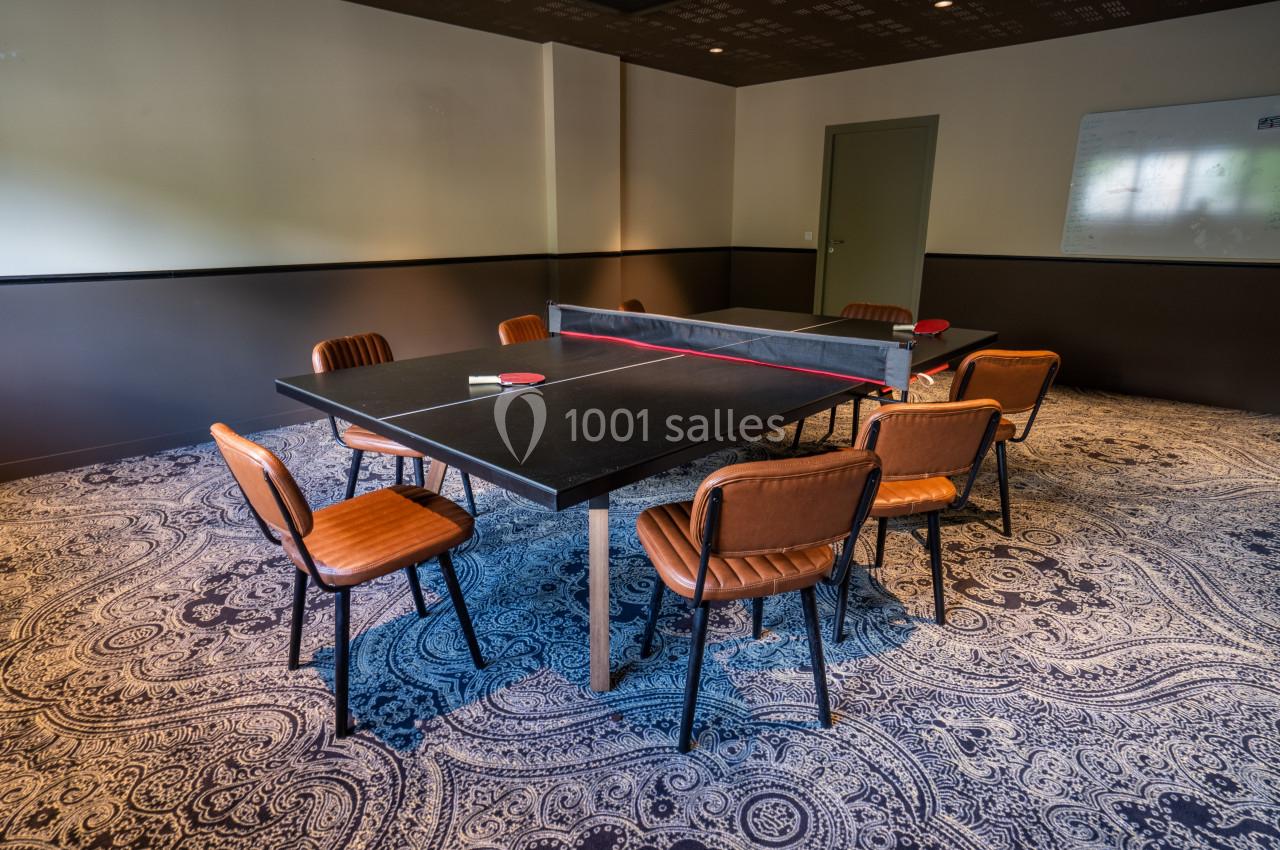 Salle avec une table de ping-pong noire entourée de chaises en cuir marron, tapis à motifs et tableau blanc au mur.