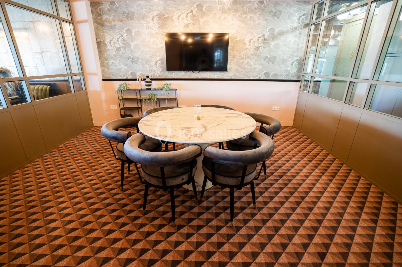 Salle de réunion avec table ronde en marbre, chaises rembourrées et écran mural, décorée de tons neutres et chaleureux.