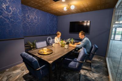 Salle de réunion avec table en bois foncé, six chaises grises, tableau blanc et écran mural.
