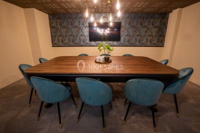 Salle de réunion avec table en bois foncé, six chaises grises, tableau blanc et écran mural.