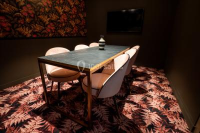 Salle de réunion avec table en bois foncé, six chaises grises, tableau blanc et écran mural.