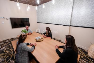 Salle de réunion avec table en bois foncé, six chaises grises, tableau blanc et écran mural.