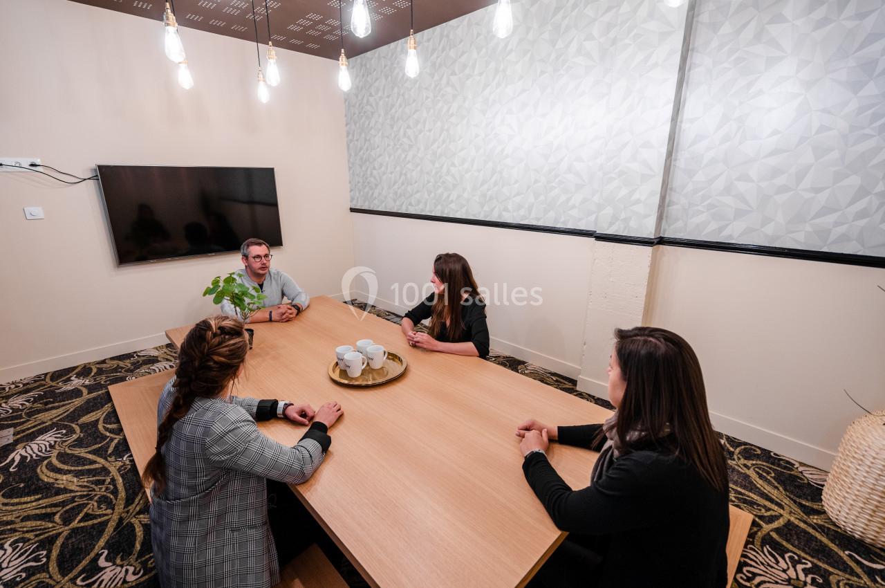 Quatre personnes discutent autour d'une table en bois dans une salle de réunion moderne avec un écran mural.