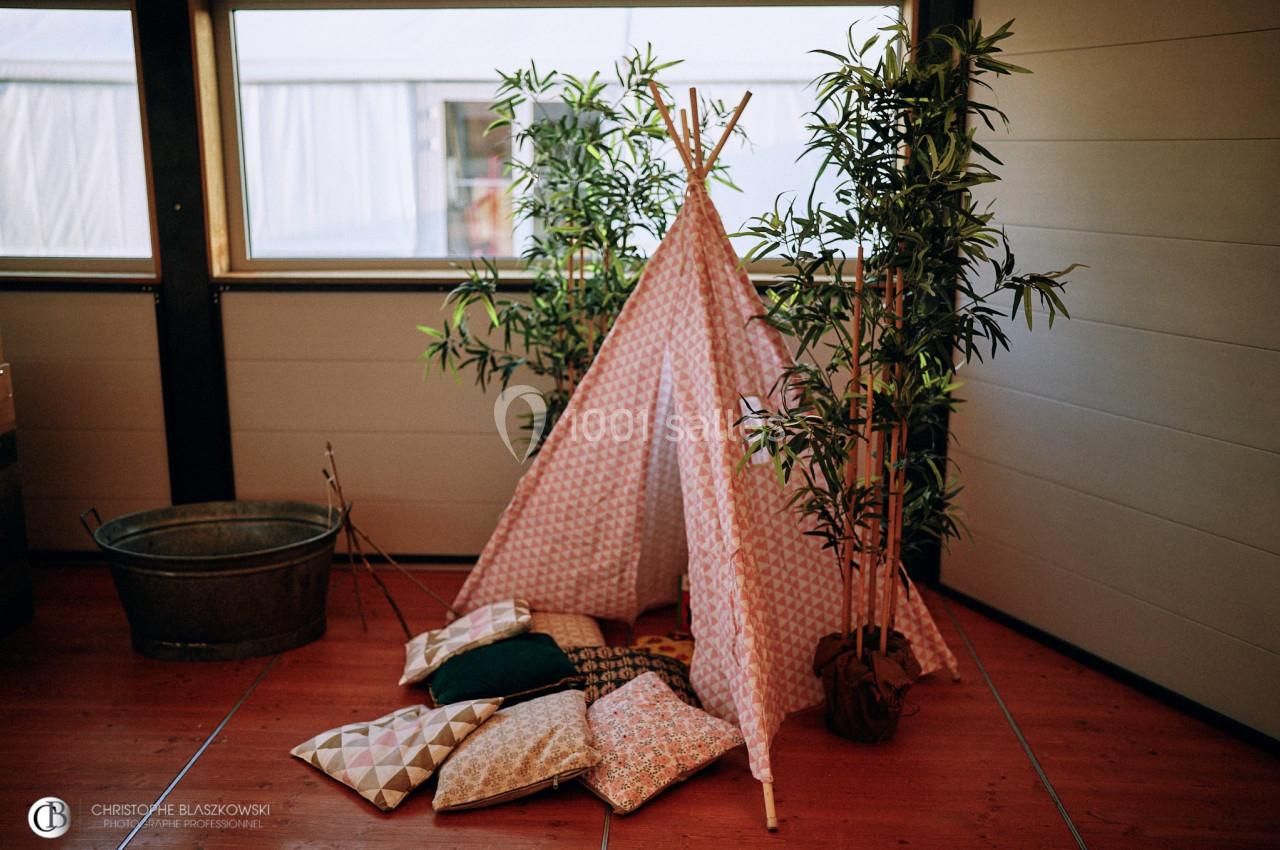 Tente décorative en tissu géométrique entourée de plantes en pot, avec des coussins colorés posés au sol.