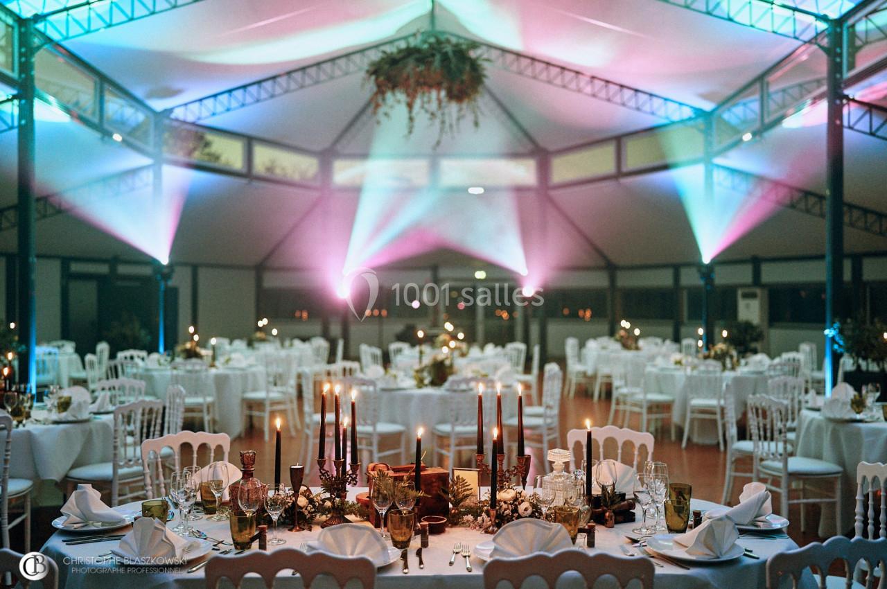 Salle de réception décorée avec des tables dressées, éclairage coloré et centre de table floral.
