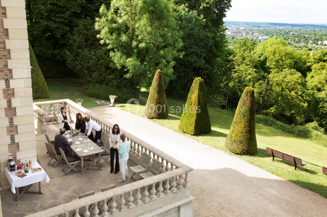 Personnes réunies autour d'une table sur une terrasse surplombant un jardin arboré avec vue sur une vallée.