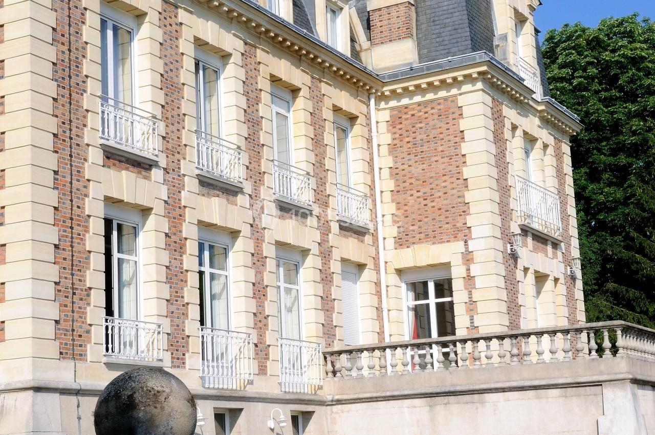 Façade d'un bâtiment ancien en briques et pierre, avec balcons et toit mansardé, entouré de verdure.