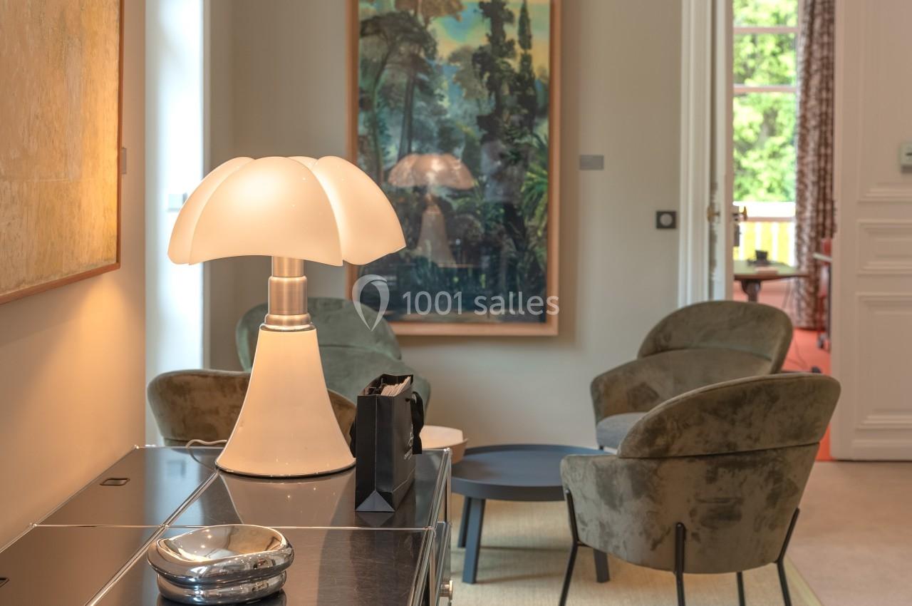 Lampe design blanche sur un meuble, avec un salon en arrière-plan comprenant fauteuils et table basse.