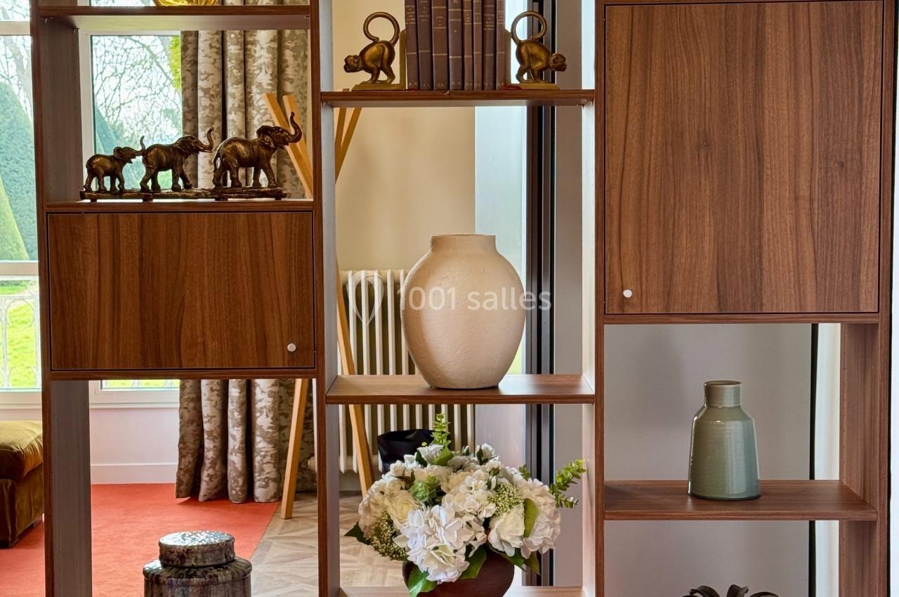 Étagère en bois avec objets décoratifs variés, dont vases, livres, figurines et plantes, dans une pièce lumineuse.