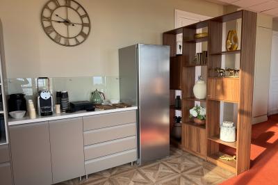 Coin cuisine moderne avec micro-ondes, cafetière, réfrigérateur, étagères en bois et horloge murale.