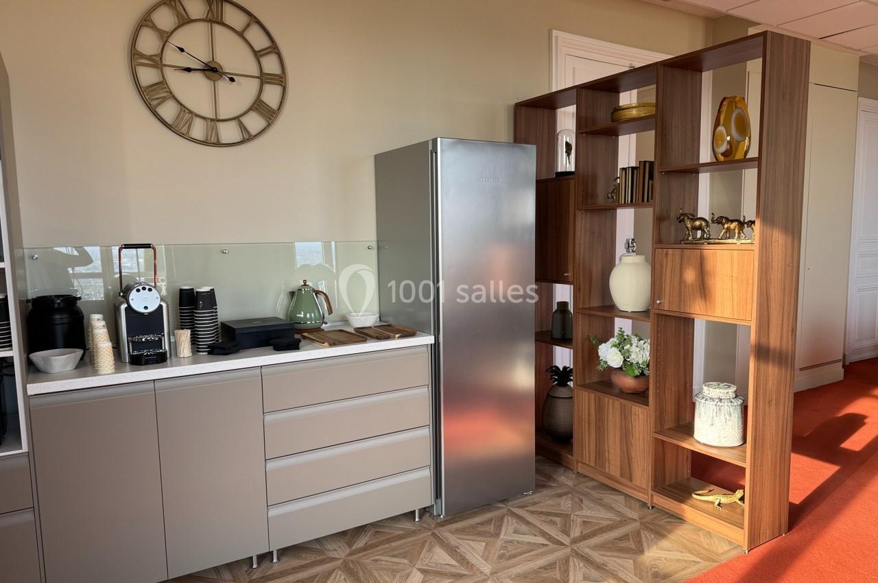 Cuisine moderne avec comptoir, machine à café, réfrigérateur inox et étagère en bois décorée d'objets.