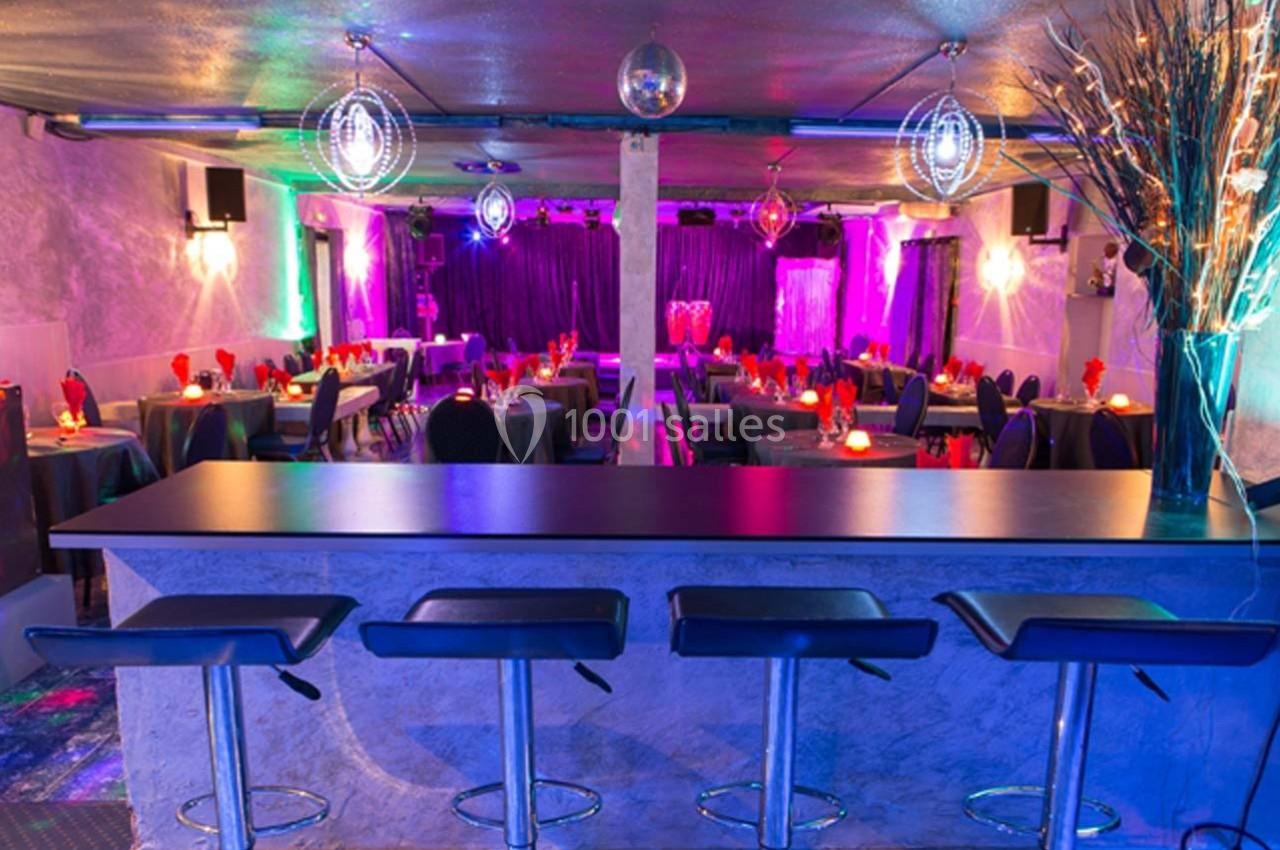 Salle colorée avec tables dressées, bar avec tabourets au premier plan et éclairage tamisé avec boules disco.