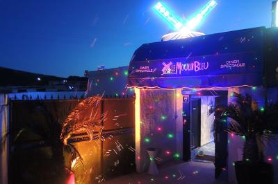 Tables rondes dressées avec nappes blanches, serviettes roses et verres, disposées en extérieur sous des parasols.