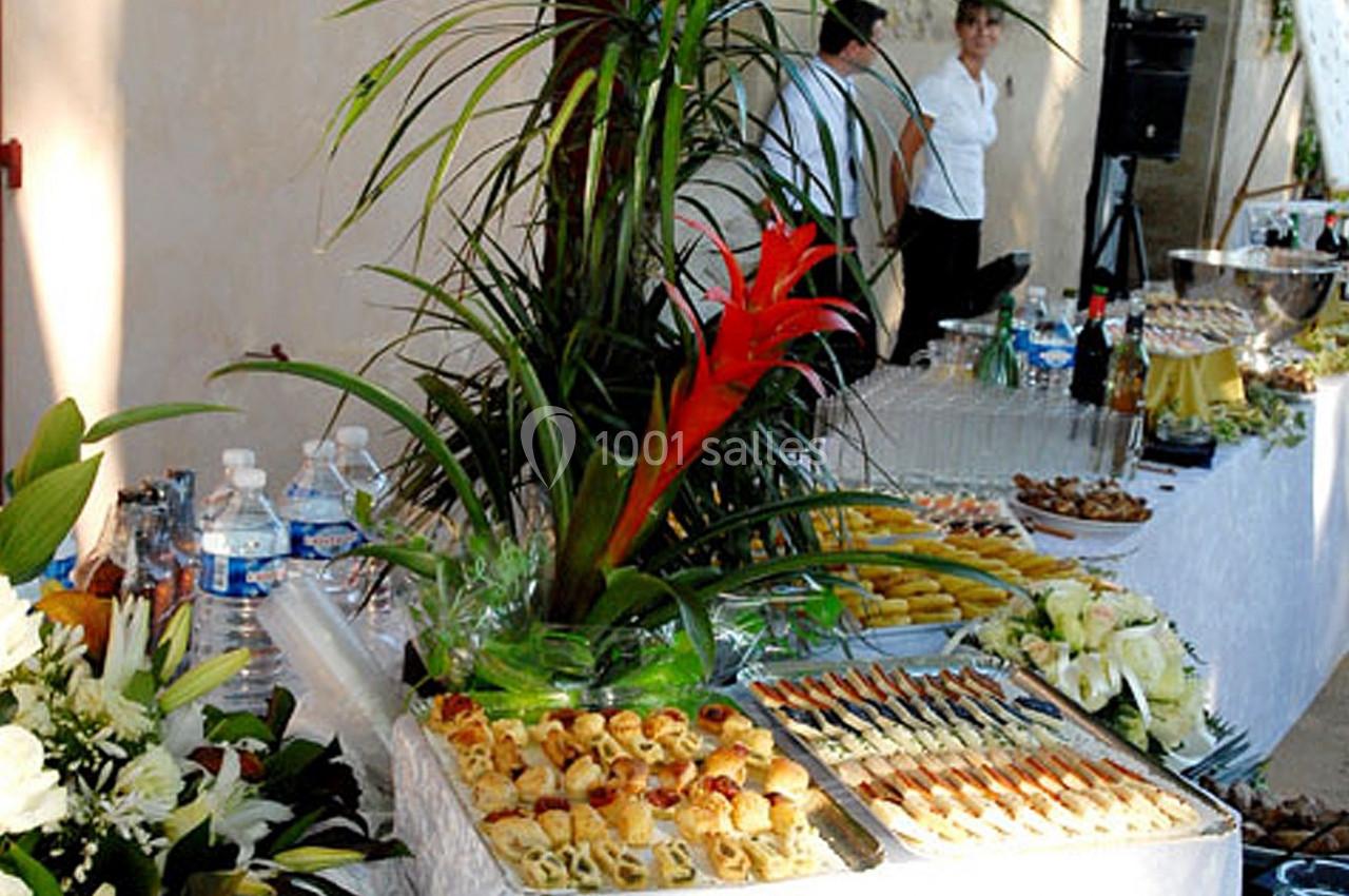 Buffet garni de plats variés, fleurs décoratives et boissons disposés sur une table blanche en extérieur.