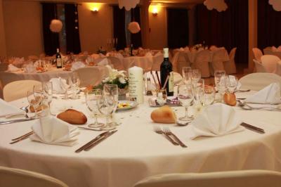 Tables rondes dressées avec nappes blanches, serviettes roses et verres, disposées en extérieur sous des parasols.
