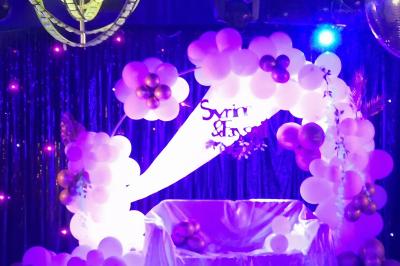 Tables rondes dressées avec nappes blanches, serviettes roses et verres, disposées en extérieur sous des parasols.