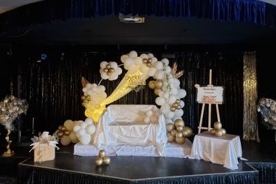 Tables rondes dressées avec nappes blanches, serviettes roses et verres, disposées en extérieur sous des parasols.