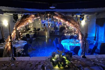 Tables rondes dressées avec nappes blanches, serviettes roses et verres, disposées en extérieur sous des parasols.