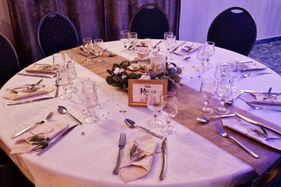 Tables rondes dressées avec nappes blanches, serviettes roses et verres, disposées en extérieur sous des parasols.