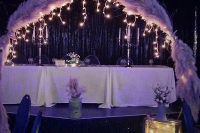 Tables rondes dressées avec nappes blanches, serviettes roses et verres, disposées en extérieur sous des parasols.