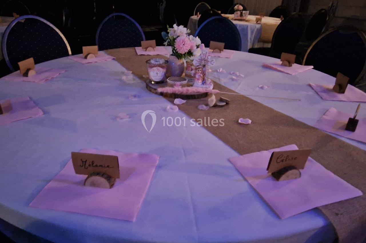 Table ronde décorée pour un événement, avec nappes, marque-places, fleurs et bougies au centre.
