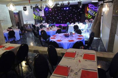 Tables rondes dressées avec nappes blanches, serviettes roses et verres, disposées en extérieur sous des parasols.