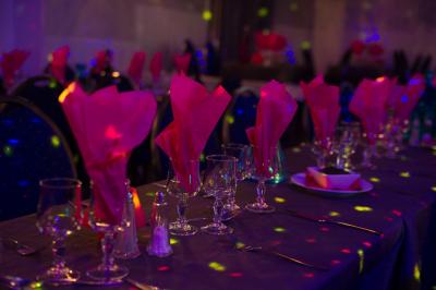 Tables rondes dressées avec nappes blanches, serviettes roses et verres, disposées en extérieur sous des parasols.