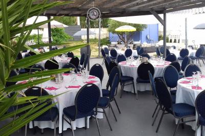 Tables rondes dressées avec nappes blanches, serviettes roses et verres, disposées en extérieur sous des parasols.