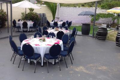 Tables rondes dressées avec nappes blanches, serviettes roses et verres, disposées en extérieur sous des parasols.
