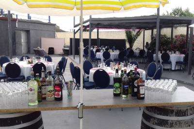 Tables rondes dressées avec nappes blanches, serviettes roses et verres, disposées en extérieur sous des parasols.