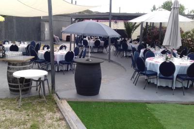 Tables rondes dressées avec nappes blanches, serviettes roses et verres, disposées en extérieur sous des parasols.