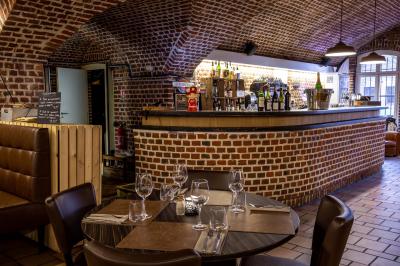 Salle de restaurant avec murs en briques, bar éclairé en arrière-plan et table dressée au premier plan.