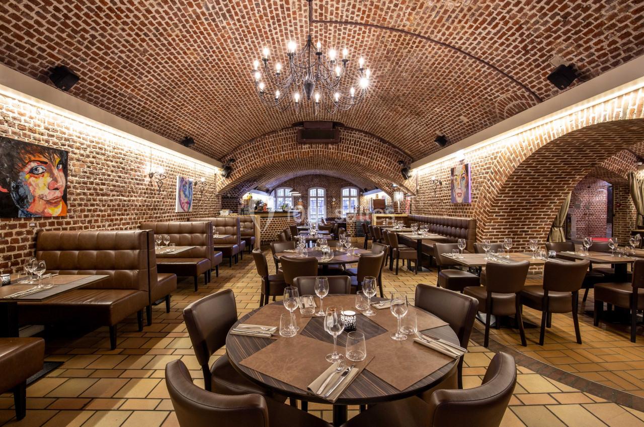 Salle de restaurant avec voûtes en briques, tables dressées, banquettes en cuir et éclairage chaleureux.