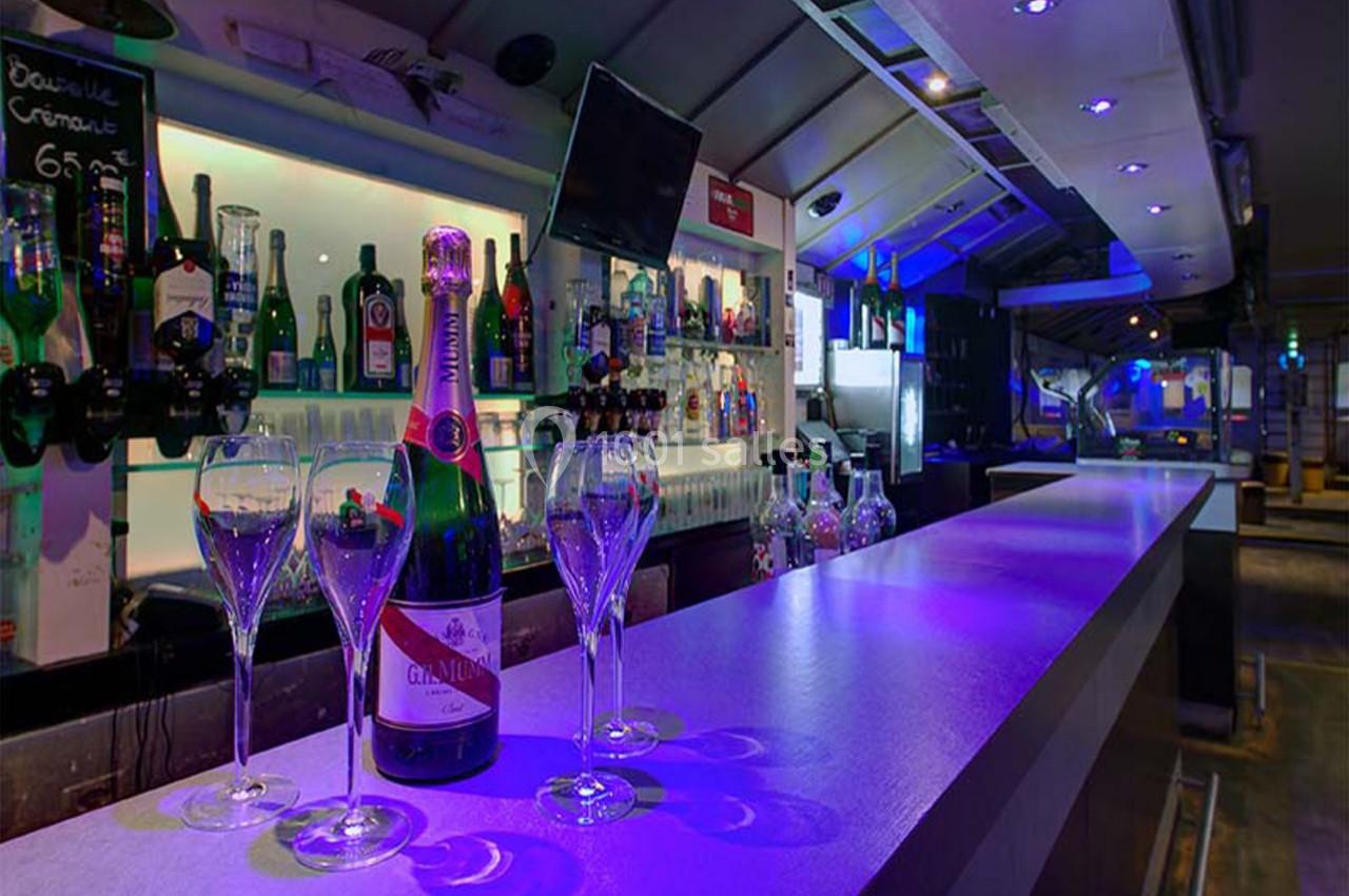 Bar moderne avec comptoir éclairé, bouteilles alignées en arrière-plan et flûtes de champagne disposées au premier plan.