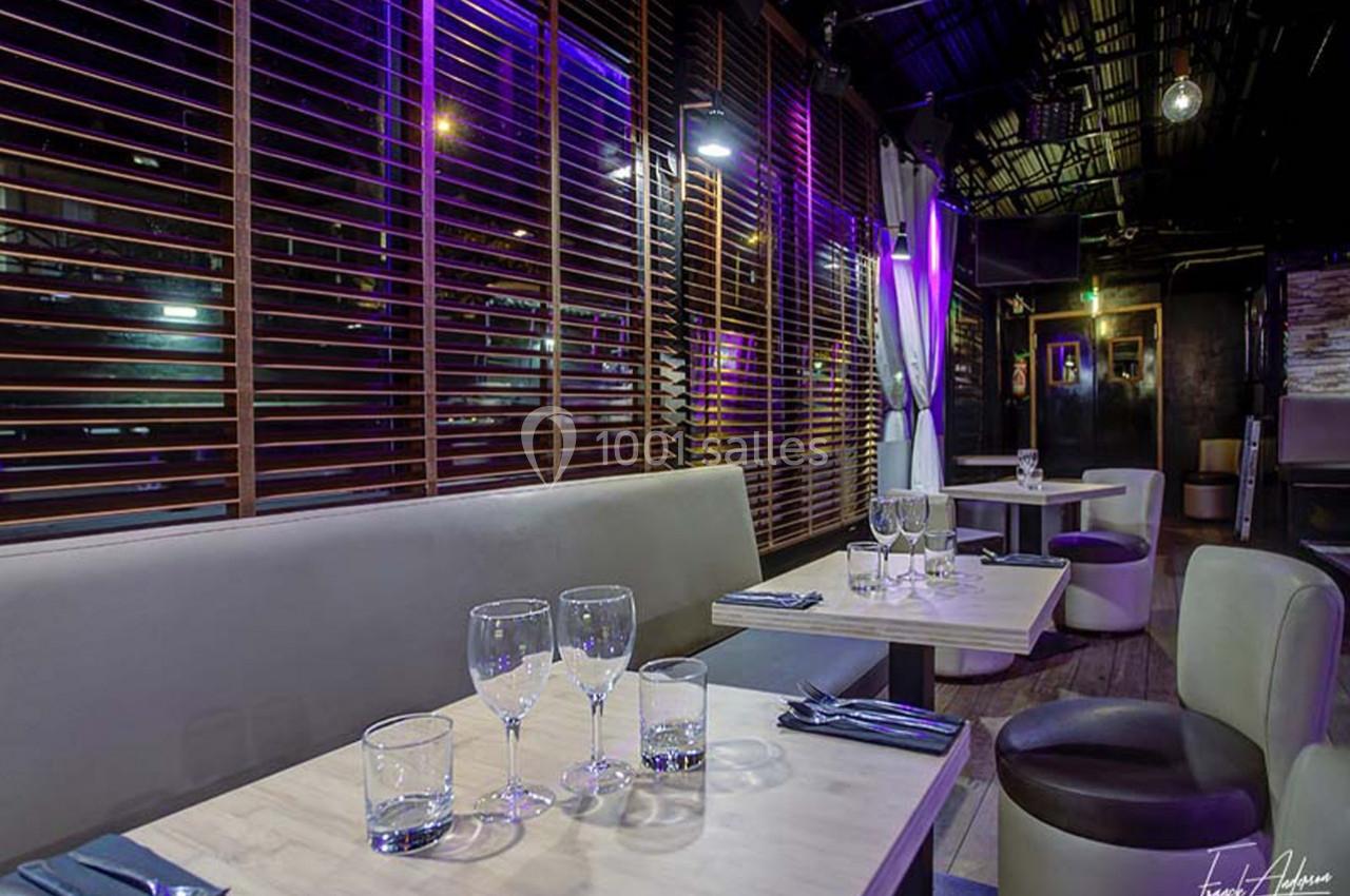 Salle de restaurant moderne avec banquettes, tables dressées et éclairage violet tamisé.