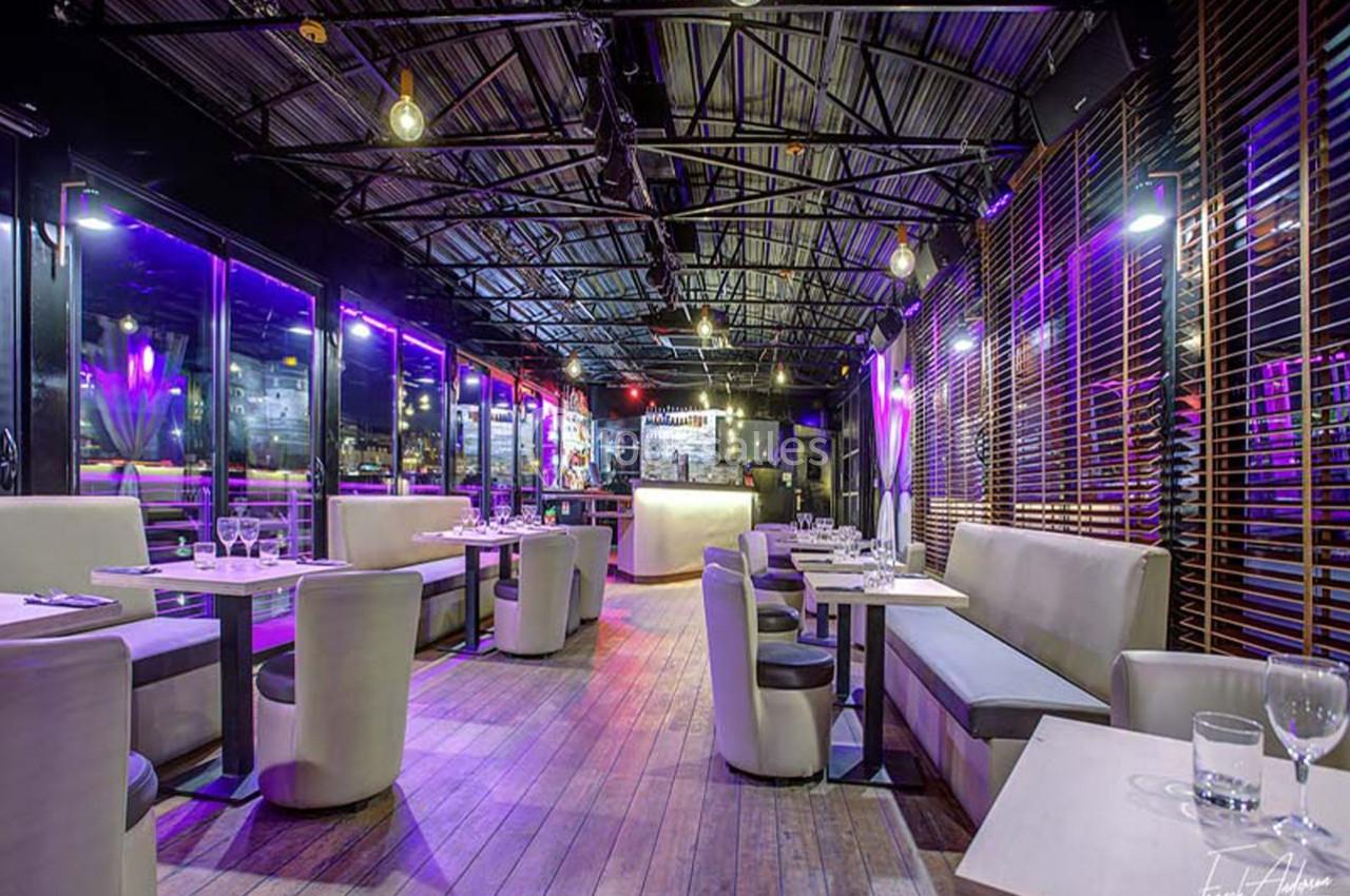 Salle de restaurant moderne avec tables dressées, éclairage tamisé et grandes baies vitrées donnant sur l'extérieur.