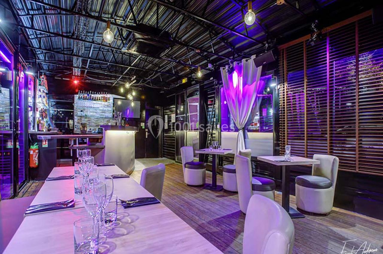 Salle de restaurant moderne avec éclairage coloré, tables dressées et ambiance tamisée.