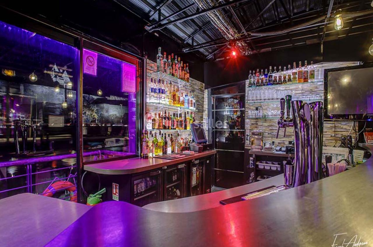 Comptoir de bar moderne avec étagères remplies de bouteilles, éclairage coloré et équipements de service.