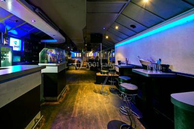 Salle de club vide avec éclairage bleu, miroirs sur les murs et bar en arrière-plan.