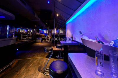 Salle de club vide avec éclairage bleu, miroirs sur les murs et bar en arrière-plan.