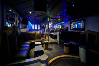 Salle de club vide avec éclairage bleu, miroirs sur les murs et bar en arrière-plan.